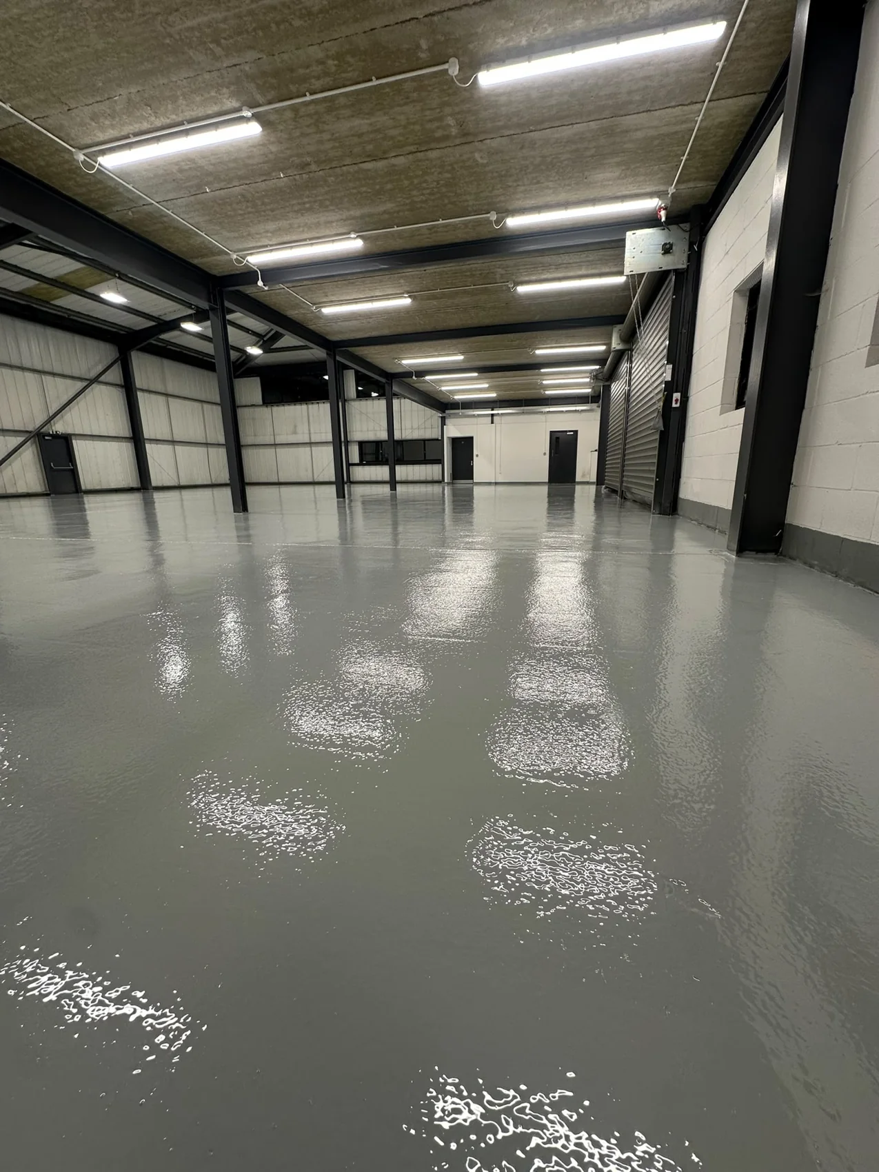 A grey floor coating across an open steel-framed warehouse